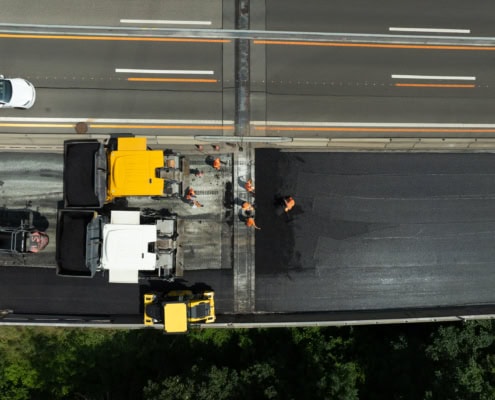 Équipe de travailleurs effectuant des travaux de bitumage sur une route avec des camions de construction.