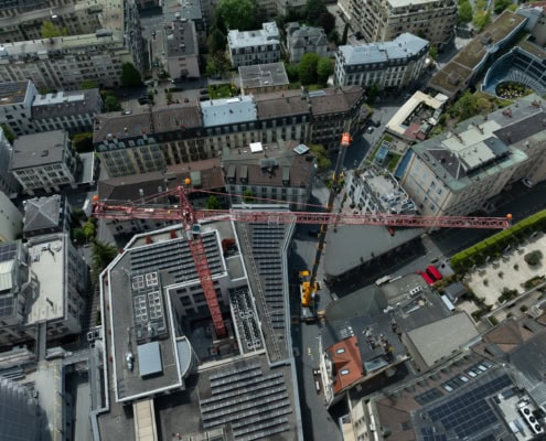Vue aérienne d'un chantier de construction avec une grue rouge sur un bâtiment urbain.