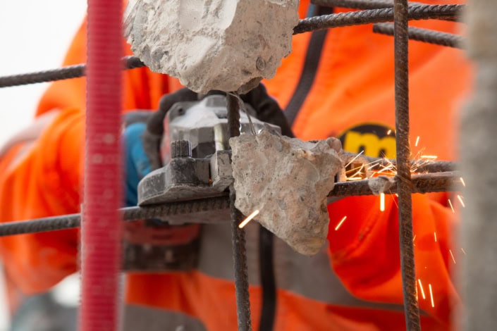 Travailleur en construction utilisant une meuleuse sur une grille métallique rouillée.