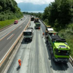 Camions de construction et ouvriers effectuant des travaux sur une autoroute en pleine journée.