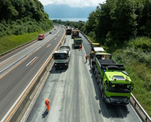 Camions de construction et ouvriers effectuant des travaux sur une autoroute en pleine journée.