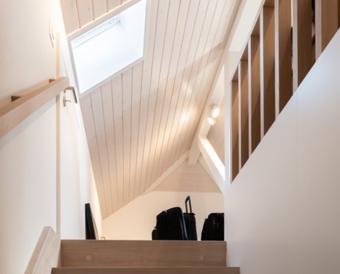 Escalier en bois menant à un espace avec un plafond en bois clair et des valises noires au sommet.