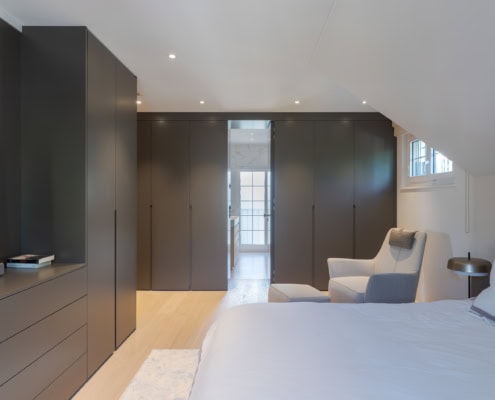Chambre à coucher moderne avec un lit, un fauteuil et des armoires sombres intégrées.
