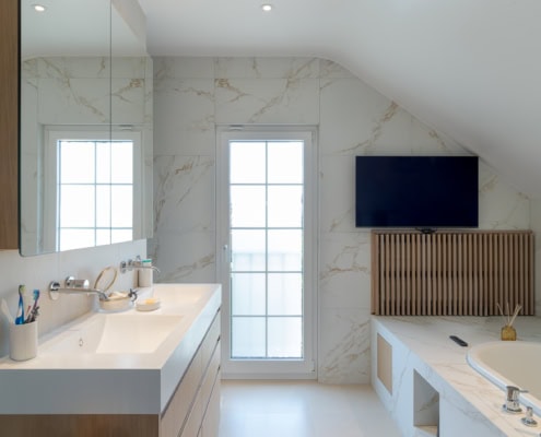 Salle de bain moderne avec un miroir, un lavabo et une baignoire, décorée de carreaux en marbre.