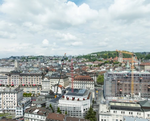 Vue aérienne de la ville de Lausanne avec des bâtiments et des grues de construction visibles.