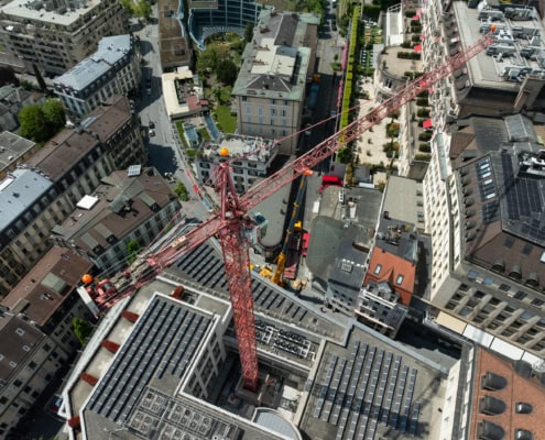 Grue de construction rouge surplombant un site urbain avec des bâtiments environnants.