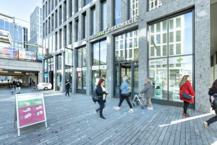 Pharmacie Medbase moderne à Lausanne avec clients et passants en mouvement.