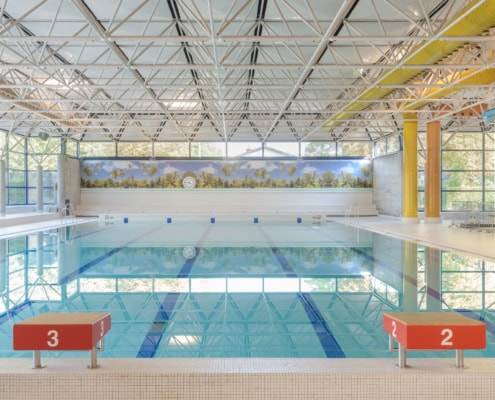 Vue d'une piscine intérieure avec des lignes de nage et une structure en acier au plafond.