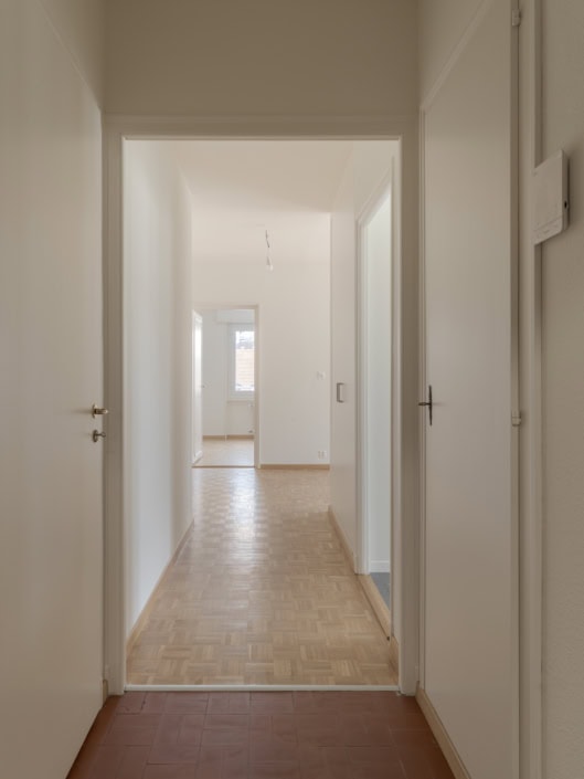Intérieur d'un appartement lumineux avec parquet en bois clair et murs blancs épurés.