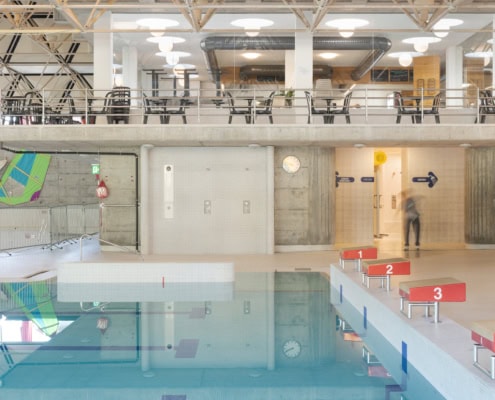 Intérieur d'une piscine avec des planches de surf colorées accrochées aux murs et un sol réfléchissant.