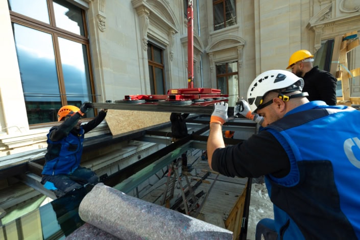 Travailleurs en construction installant une grande fenêtre sur un bâtiment historique.