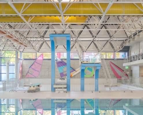 Intérieur d'une piscine avec des planches de surf colorées accrochées aux murs et un sol réfléchissant.