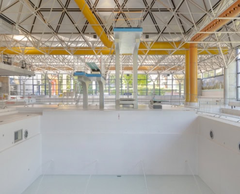 Vue intérieure d'une piscine avec plongeoirs et un plafond en structure métallique.