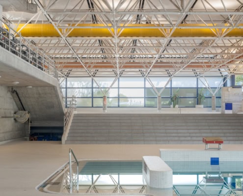 Intérieur d'une piscine moderne avec des murs en béton et une structure en acier visible au plafond.