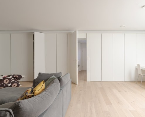 Un salon moderne avec un canapé gris et des portes coulissantes blanches ouvertes.